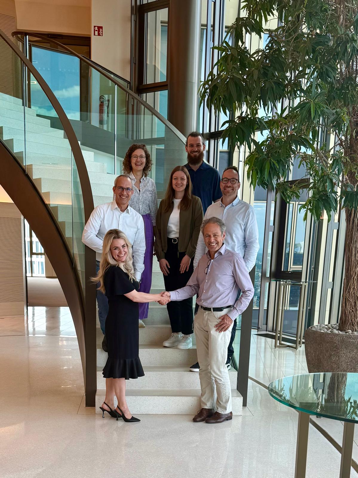 Geocledian and PwC Germany are partnering up: Six businesspeople stand on a staircase, the woman and man at the front shake hands.